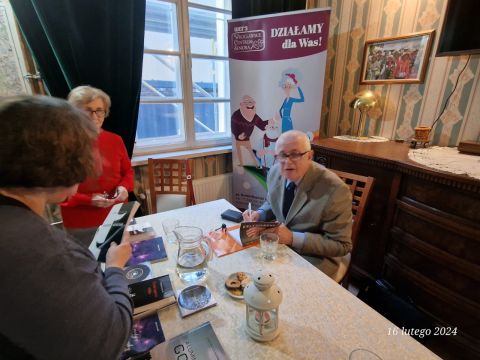 Na zdjęciu przy stole siedzi autor i podpisuje swoje książki