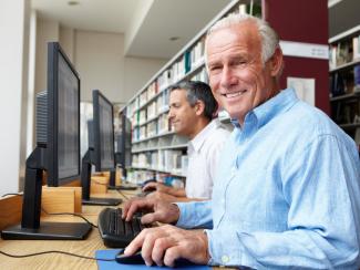 Na zdjęciu widać dwóch seniorów siedzących przed komputerem w bibliotece