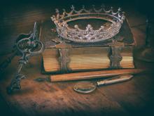 Na zdjęciu widać starą księgę, koronę, klucz i pióro. 