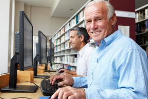 Na zdjęciu widać dwóch seniorów siedzących przed komputerem w bibliotece