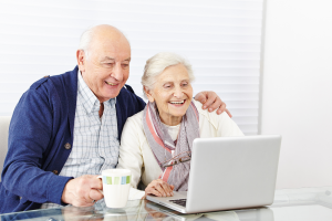 Senior i Seniorka siedzą przy stole i korzystają na laptopa