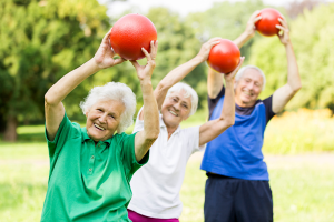 Trójka seniorów w parku ćwiczy gimnastykę z piłkami w rękach