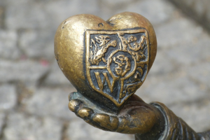 pixabay-dloń wrocławskiego krasnala trzyma serce z herbem Wrocławia - fragment figurki miejskiej na tle kostki brukowej