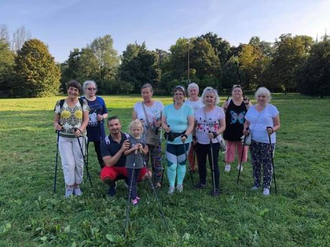 na zdjęciu w plenerze grupa seniorów z z nordic walking z trenerem